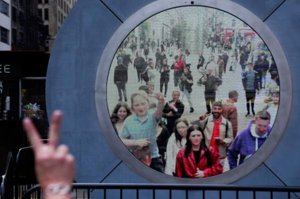 People in both New York and Dublin, Ireland, wave and signal at each other while looking at a livestream view of one another as part of an art installation on the street in New York, Tuesday, May 14, 2024. (AP Photo/Seth Wenig)