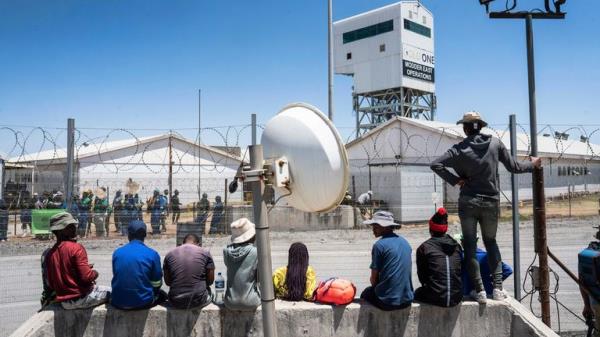 Fellow mineworkers look over the entrance of a goldmine in Springs, near Johannesburg, South Africa Wednesday, Oct. 25, 2025. A company official says more than 100 miners have escaped from the mine after being held underground for three days by fellow employees in a unio<em></em>n dispute. (AP Photo)