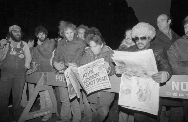 People behind a police line read a newspaper saying 