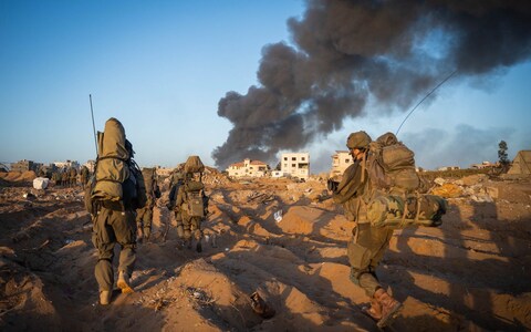 Israeli forces advance towards a building wher<em></em>e dark smoke is billowing