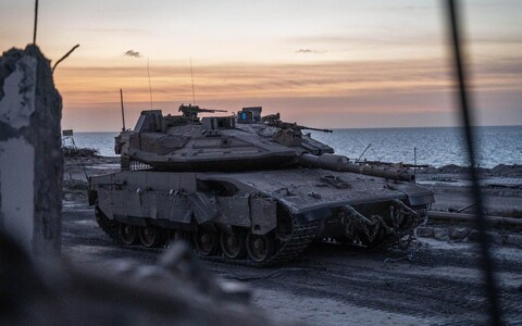 An Israeli Merkava IV tank rolls along the sands as the sun sets