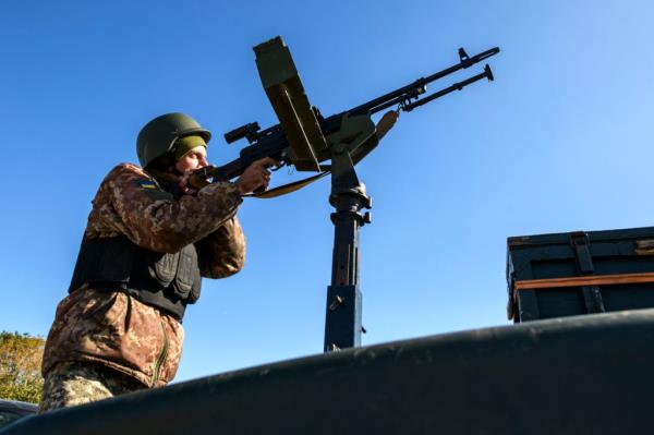 A Ukrainan soldier stands behind a mounted automatic weapon pointed toward the sky.