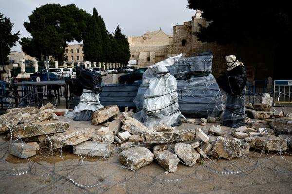 A Christmas installation outside the Church of the Nativity features covered figures standing amid rubble surrounded by a razor wire. 