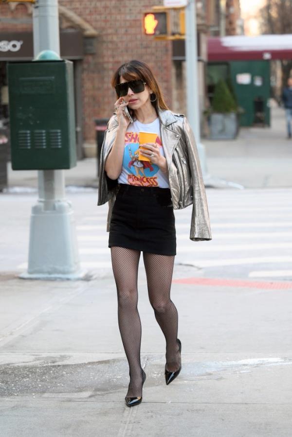 Hilaria Baldwin wearing a mini skirt and me<em></em>tallic leather jacket, holding a coffee cup on a New York City sidewalk.