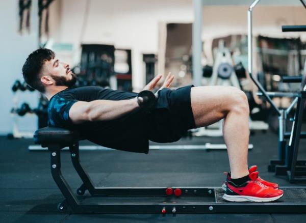 muscular man doing barbell hip thrusts at the gym