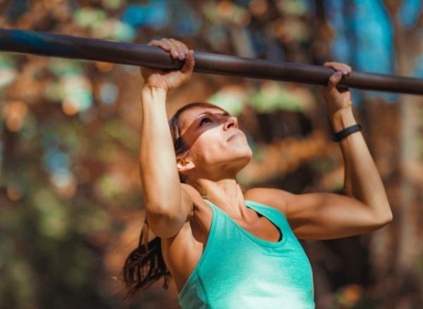 fit woman doing pull-ups outside, co<em></em>ncept of bodyweight workout to slow muscle aging