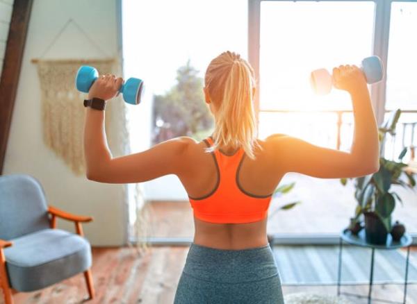 woman doing dumbbell shoulder press exercise in living room, co<em></em>ncept of at-home workouts for beginners