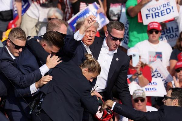 Do<em></em>nald Trump holds up a fist with his face bloodied as Secret Service agents rush him off stage.