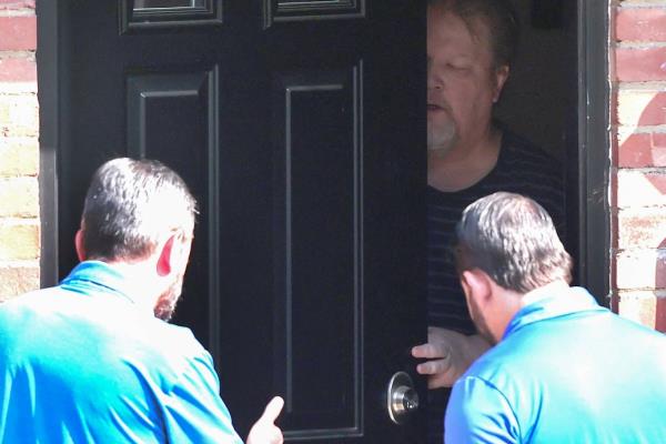 A man speaks with federal investigators through a slightly open front door.