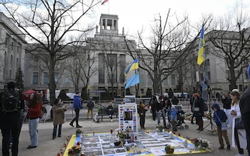 The embassy is a large, imposing, grey building in the Soviet style. There are trees in front of it and a few protesters flying Ukrainian flags and displaying printed material a<em></em>bout the war