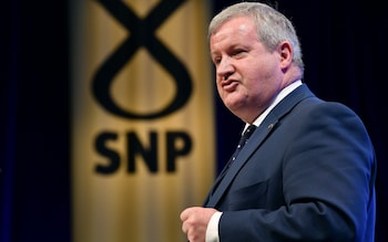 Mr Blackford wears a suit and tie and speaks in front of an SNP logo