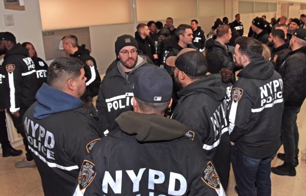 A group of many NYPD officers in black jackets standing outside Bronx Criminal Courthouse for an arraignment.