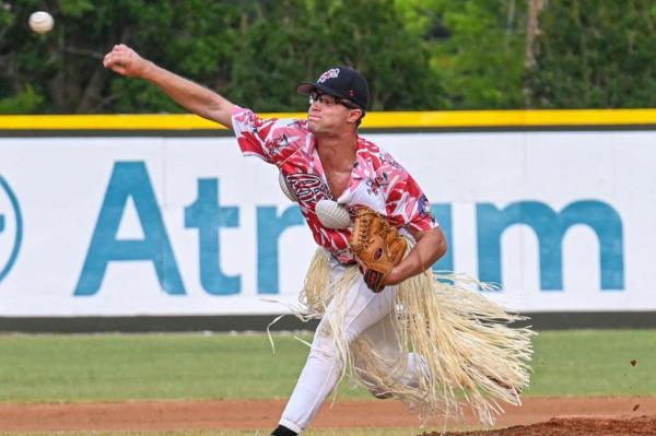 A ba<em></em>seball pitcher in a Hawaiian shirt and grass hula skirt throws a ball.