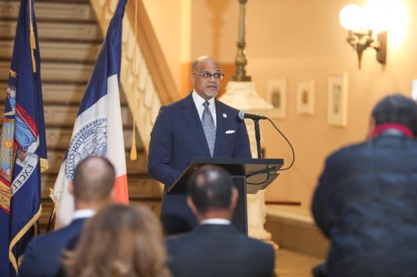  NYC Dept of education Chancellor David C. Banks speaks to the press and public at the Tweed Building in Manhattan, standing behind a lectern with a microphone, in front of city and state flags and a staircase.