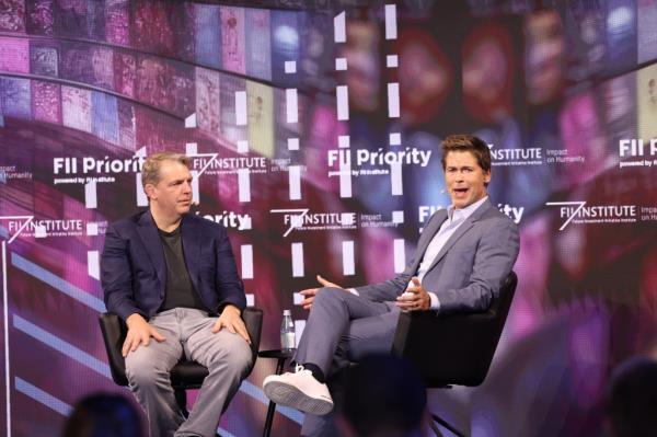 Rob Lowe in a chair on a stage talking to a casually-dressed man.