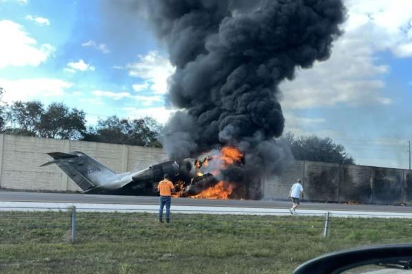 Two bystanders watch as a Bombardier Challenger 600 jet is engulfed in flames after it crashed on I-75 in Florida on Friday afternoon.