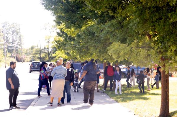 Migrants wait across from the shelters for their children to be dro<em></em>pped off from school