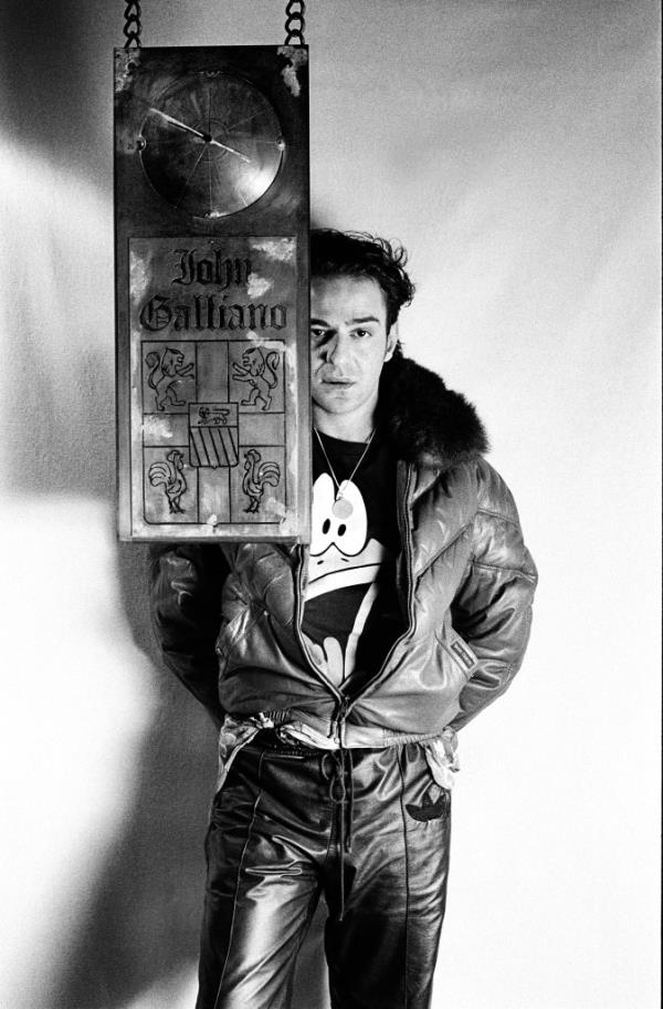 John Galliano standing in front of a sign that features his name