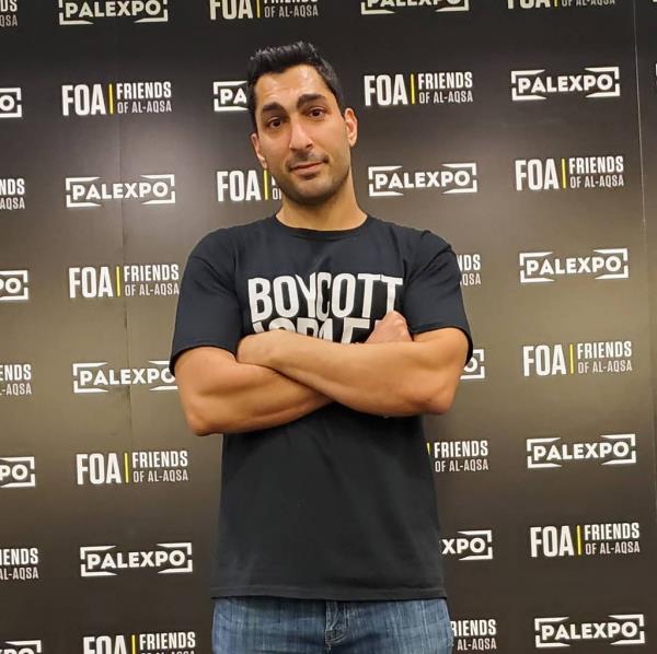 Remi Kanazi standing in front of a wall with his arms crossed at an Anti-Israel protest