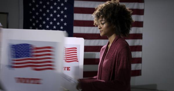 Young mixed-race woman ready to vote with blurred voting booth in foreground, being removed.