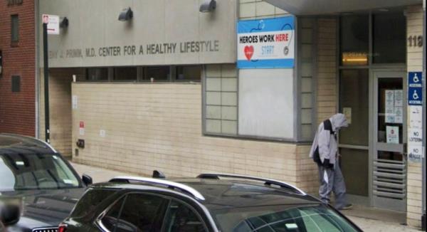 A sidewalk view of a drug treatment center wher<em></em>e a man wearing shabby clothes stands at the door.