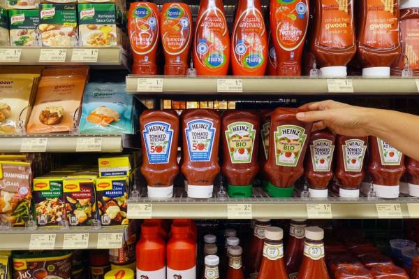 Hand reaching for a Heinz ketchup bottle in grocery store.