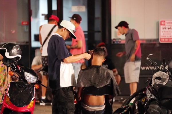 One apparent migrant giving another migrant a haircut on the sidewalk outside of the Roosevelt Hotel in New York, NY on September 6, 2023. 