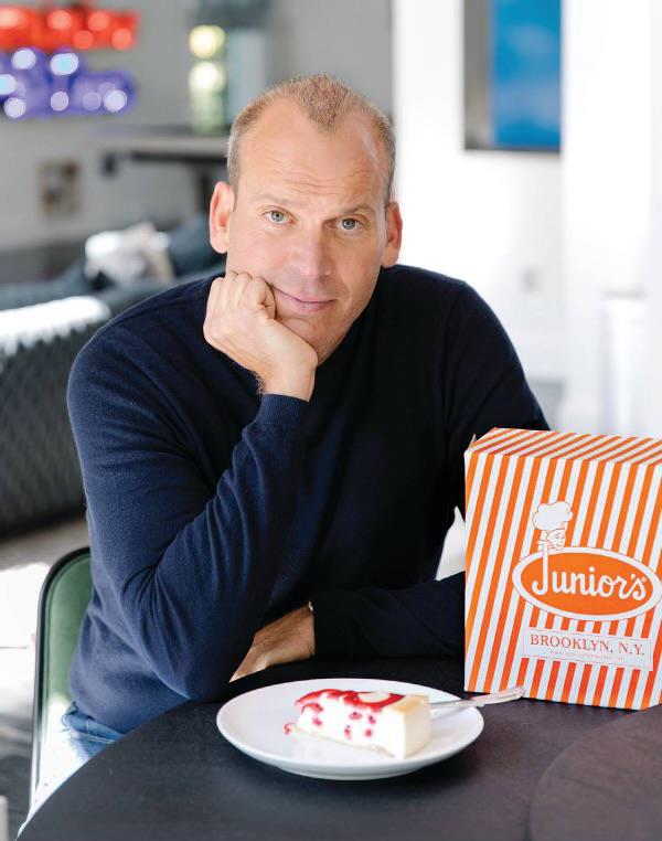 Junior's Restaurant owner, Alan Rosen, sitting at a table with a plate of cake and a box of food