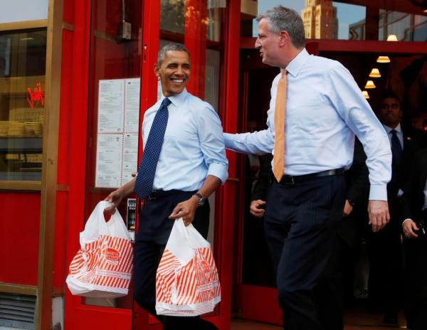 President Barack Obama holding two bags of cheesecake from Junior's Restaurant, standing next to Democratic Mayoral candidate Bill de Blasio in Brooklyn