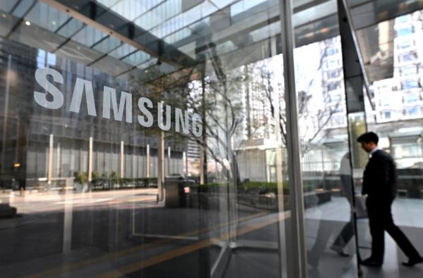 Man walking past the Samsung logo on a glass door at the company's Seocho building in Seoul, suggesting a rise in their profits due to chip price recovery.