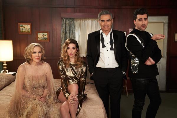 Moira (Catherine O'Hara), Alexis (Annie Murphy), Johnny (Eugene Levy), David (Dan Levy) standing in a room smiling. 