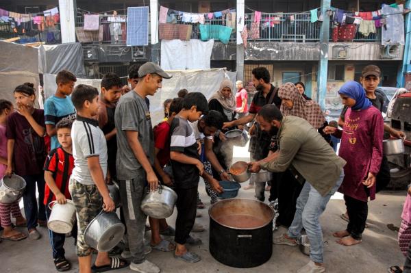 Children queue with pots to receive food aid from a kitchen at the Abu Zeitun school run by the UN Relief and Works Agency for Palestine Refugees (UNRWA)