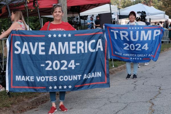 Two supporters of former President Do<em></em>nald Trump hold banners that say SAVE AMERICA 2024 and TRUMP 2024 as a large crowd of Trump supporters rallied at the Fulton County Jail in Atlanta wher<em></em>e the former president was to turn himself in after being indicted on charges related attempting to overturn the results of the 2020 presidential election, which he lost to Joe Biden.