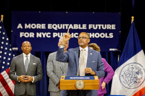 New York City Department of Education Chancellor David C. Banks speaking at a press co<em></em>nference a<em></em>bout building a more equitable future for NYC public schools, pointing up while standing at a podium.