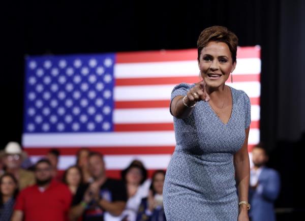 Arizona Senate candidate Kari Lake pointing at a flag, greeting supporters at a campaign event in Tucson, Arizona