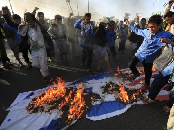 Houthi members and supporters stomp on an Israeli and American flag they set on fire. 