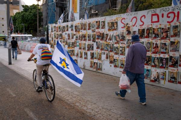 Passersby observe the photos of hostages held in the Gaza Strip that are plastered to the walls 