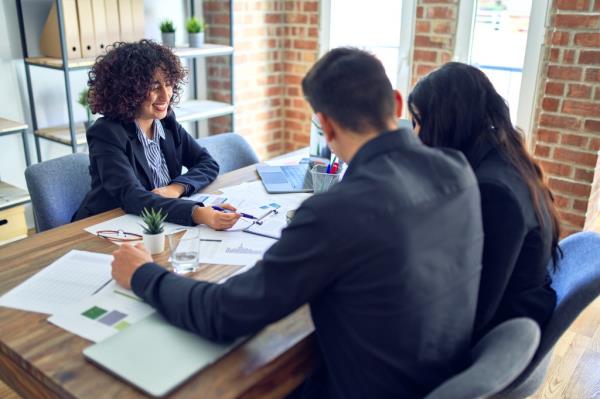 Young happy couple sitting with a real estate agent, signing mortgage loan docu<em></em>ments at a bank