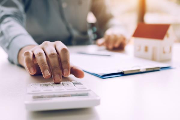 Businessman's finger pressing on a calculator for calculating house mortgage budget in the office