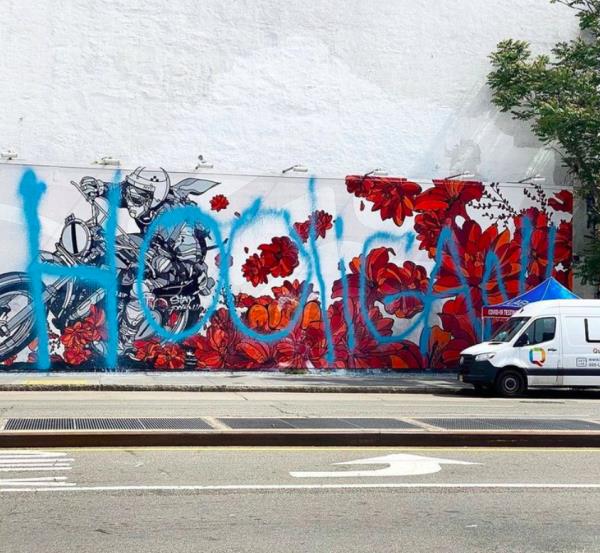 David Flores’s flowery, red mural of a motorcycle  on the Bowery wall with a large blue graffiti tag over it.