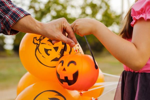 Little kid girl trick or treating on Halloween. man's hand puts a candy in the basket