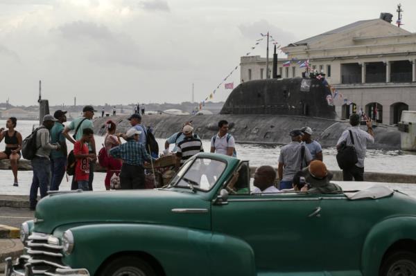 A co<em></em>nvertible American classic car drives by as people watch the Russia's Kazan nuclear-powered submarine arrive in the port of Havana, Cuba, Wednesday, June 12, 2024. A fleet of Russian warships arrived in Cuban waters Wednesday ahead of planned military exercises in the Caribbean. (AP Photo/Ariel Ley)