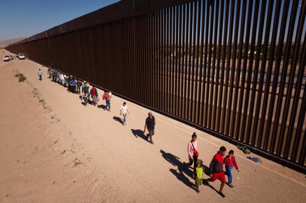 Migrants walk along the U.S.-Mexico Border wall after crossing the Rio Grande river from Ciudad Juárez, Mexico into the United States on Tuesday, October 3, 2023 in El Paso, Texas.  