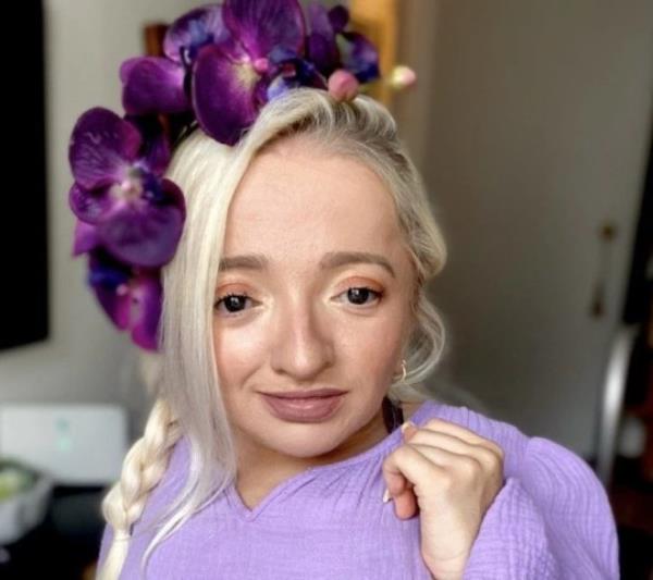 Samantha Renke at home, wearing purple flowery headwear and a lilac top.