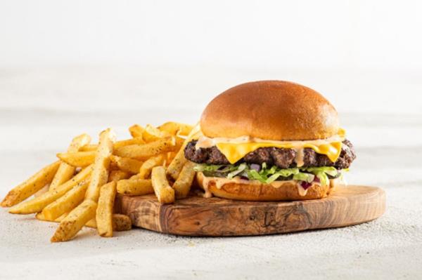 Chili's Big Smasher burger with cheese and fries on a wooden board, advertised as havin<em></em>g more beef than a Big Mac