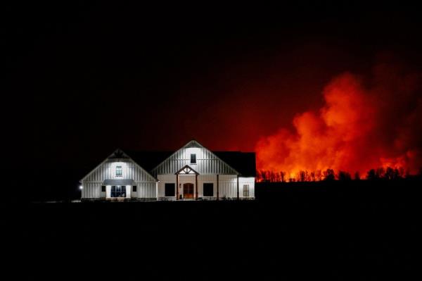 A wildfire that prom<em></em>pted evacuations burns in the distance behind a home outside of Shattuck, Oklahoma on Feb. 27, 2024. 