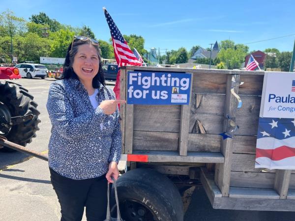 A woman, Paula Collins, standing next to a wooden trailer with flags