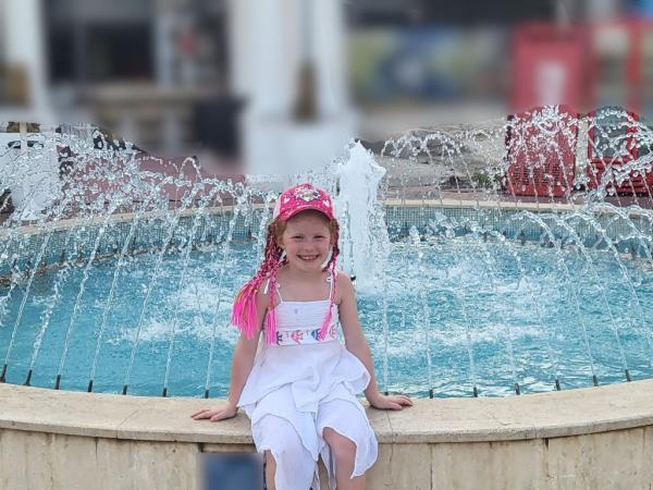 Photo of a smiling girl sitting near a fountain. 