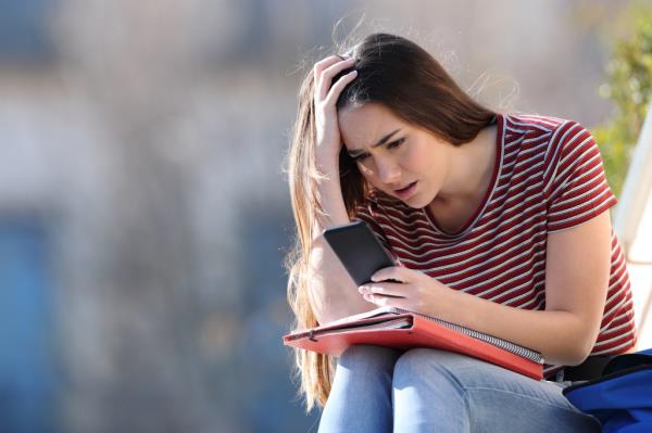 Worried female student holding her head while looking at her mobile phone on a campus