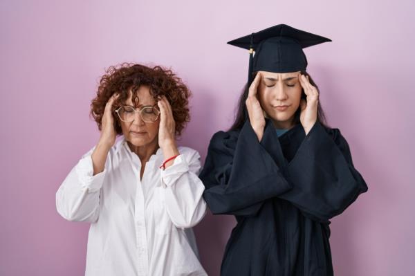 Hispanic mother and daughter in graduation caps and gowns showing signs of stress